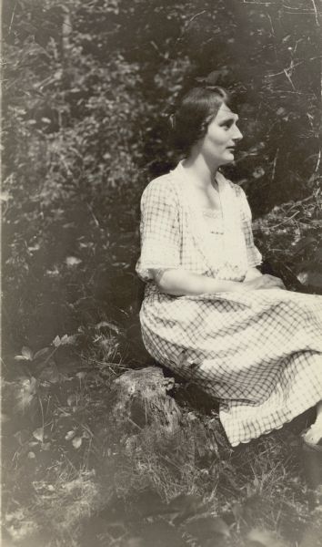 Alma Schmidt poses seated outdoors wearing a light summer dress. Her face is in profile.