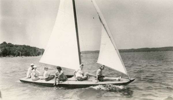 View across water of women and children sitting on the deck of the Sailing School Ship on Lake Geneva. Herb Taylor, partly obscured on the afterdeck, was the instructor.