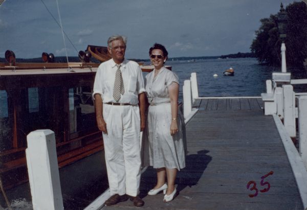 Ernst C. Schmidt and Mary Helen Anderson stand on a pier and pose next to the Black Point launch "Nepenthe."