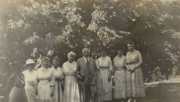 A group of nine women pose with Charles Wacker, center, on "A Sunday Afternoon - about 1914" on the lawn at Black Point. The individuals are identified, from left, as Mrs. Francis T.A. Junkin; Mrs. Otto L. [Emma Seipp] Schmidt; Mrs. Henry [Clara Seipp] Bartholomay; Mrs. Harry Williams; Mrs. Conrad [Catherine Orb] Seipp; Mr. Charles Wacker;  Rosalie Wacker (Mrs. Earle Zimmerman); Mrs. Albert [Elsa Seipp] Madlener; Mrs. Frederick Wacker; Mrs. August C. Magnus.