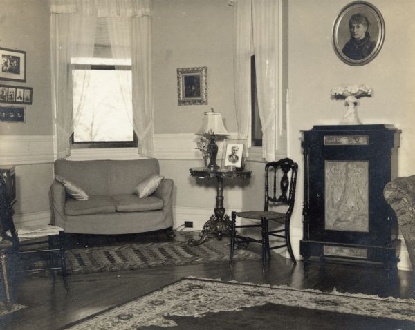 An oval portrait of Emma Seipp Schmidt hangs above a cabinet in the music room at Black Point. A modern style settee stands in the large window bay.
