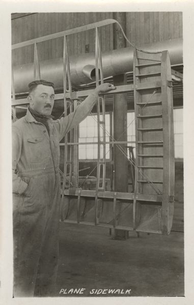 Man standing next to a Lawson Military Tractor 2 (MT2). The man is wearing a coverall worksuit and has a mustache and undercut haircut.