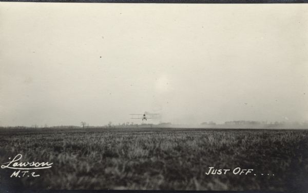Lawson Military Tractor 2 (MT2) just after it has taken off from a field, probably from the Lawson Aviation Field in Green Bay. Rear view of airplane just above the horizon in the far distance, with a narrow depth of field aimed near the airplane.