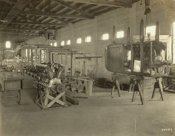 Interior of the Lawson machine shop, with two Lawson engines, one housed in part of a fuselage, the other set on a wooden support. A long wooden frame is in the background and is possibly part of the fuselage for a Lawson Air Liner.