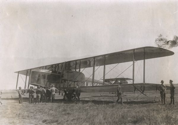 Three-quarter view from front left of a Lawson Air Liner parked in a field. Several men in uniforms are inspecting the plane.