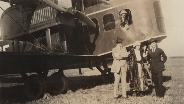 Alfred Lawson stands with Charles Cox, pilot of the Lawson Air Liner, and Cox's wife. Another woman leans out of an open window in the cockpit.