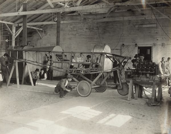 Several men are working on different parts of a Lawson Military Tractor 2 (MT2), including the interior structure of the plane, the engine, and the exterior plates in the background. The caption on the photograph reads: "Built by the Lawson Aircraft Corporation. Green Bay, Wisconsin."