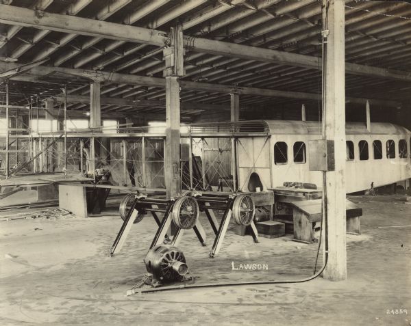 A Lawson Air Liner under construction at the Milwaukee plant. The cockpit and cabin have been enclosed with exterior plates, and the tail structure is visible. The wheel assembly is inverted on the ground in front of the tail.