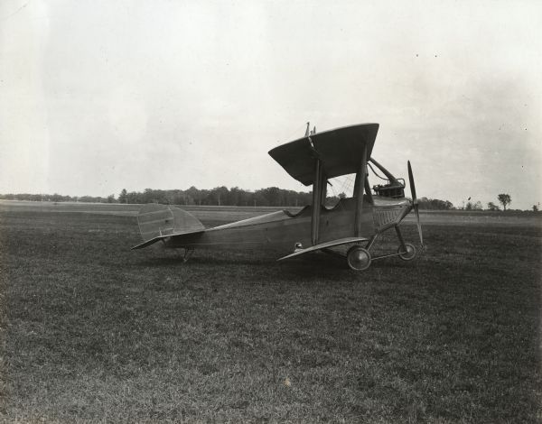 A Lawson Tractor Biplane is parked in a field, in profile. 