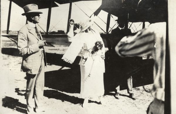 A woman, identified elsewhere as "Mrs. John Pfingsten, wife of one of the Lawson company stockholders" is preparing to christen the Lawson Air Liner. A man stands next to her holding a cigar, and might be her husband.