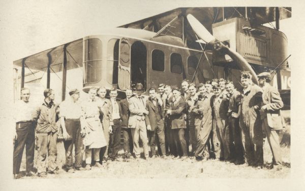 Alfred Lawson standing in the center of a large group of men, many of whom are wearing work clothes. Behind them is a Lawson Air Liner.