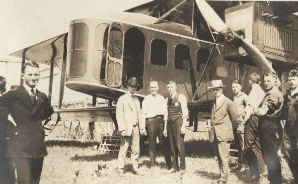Several people, including Alfred Lawson, posing in front of a Lawson Air Liner. Some of the men are wearing suits, others are wearing work clothes.