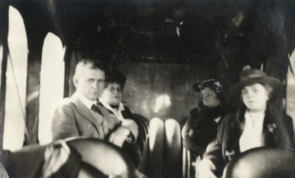 Alfred Lawson is sitting with three women inside the cabin of a Lawson Air Liner. 