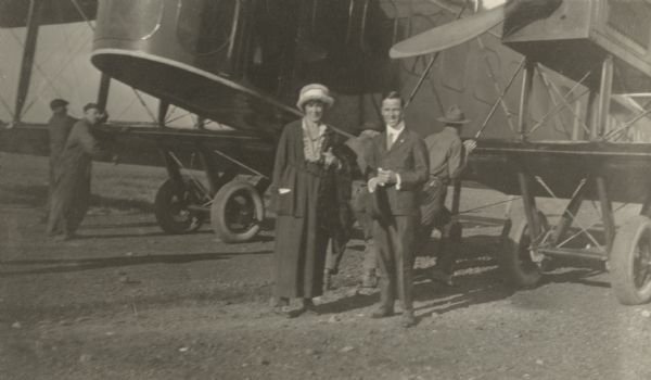 An unidentified man and woman posing in front of a Lawson Air Liner. Several men are pushing the plane backwards by the wings.