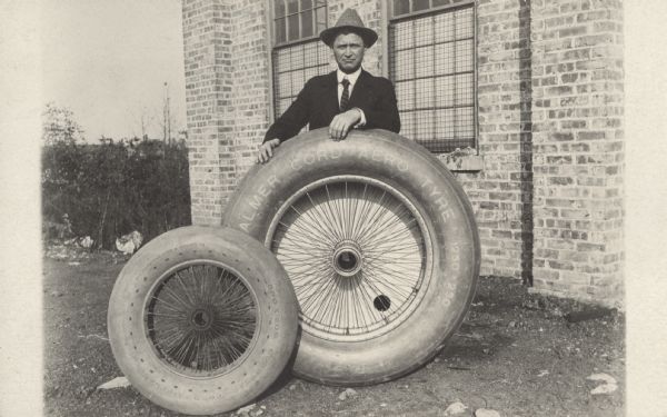 Alfred Lawson standing behind a Palmer cord aero tyre, which is sitting next to a smaller Goodyear cord tire. The smaller Goodyear tire was used for Lawson's 1919 air liner, and the larger Palmer tire was used for his 1920 Midnight Air Liner, which would provide overnight service.