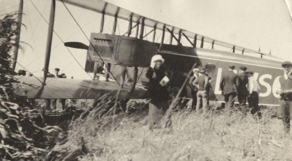 Several people standing in a field inspecting a Lawson Air Liner. A woman and a man are facing the camera in the foreground.