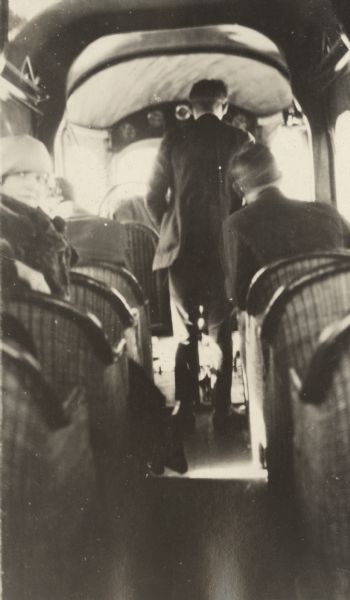 View from rear of airplane of passengers sitting inside a Lawson Air Liner. One man is standing and facing the cockpit.