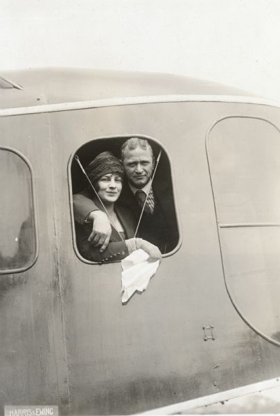 Portrait of Alfred Lawson, with his arm around the shoulders of an unidentified woman who is holding a handkerchief. They are posing while looking out of an open window from the cockpit of a Lawson Air Liner.