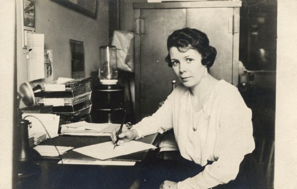 Portrait of Dorothy H. Wright sitting at a desk, holding a pen. On the back of the image she has written: "To A.W. Lawson from Dorothy H. Wright, Nov. 11 - 1920."