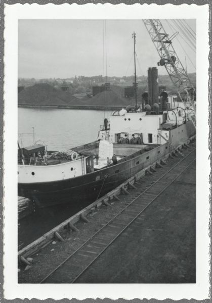 Elevated view over railroads tracks of Canadian ship with cargo of wood pulp. Sulphide bales are being unloaded and there are several men on the ship. In the background are large piles of coal.