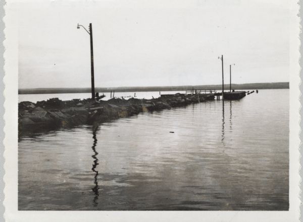 View across water towards jetty and dock, with three lampposts, from south east.