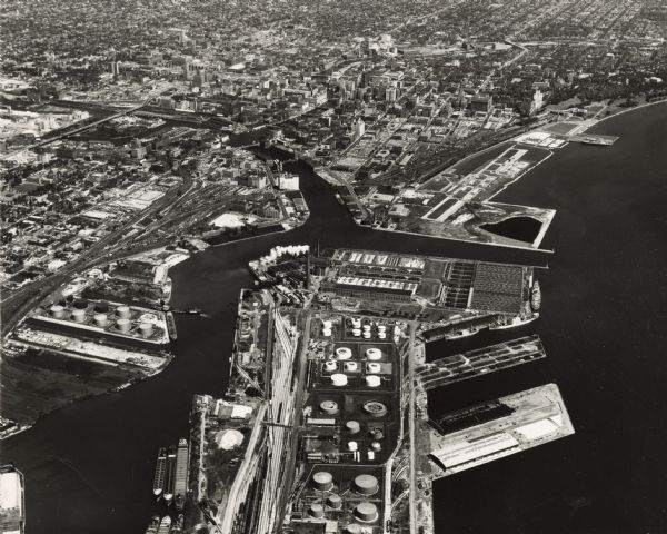 Aerial view of North and South Harbor Tracts, looking north from South Pier No. 2. There are skyscrapers in the background. there are multiple items of machinery. Ships are along the shoreline.