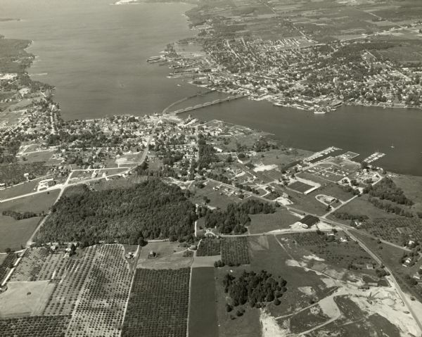 Aerial view of harbors and bridge. Farm fields are on either side of the bridge. The city of Sturgeon Bay is in the distance. There are docks along the shoreline.