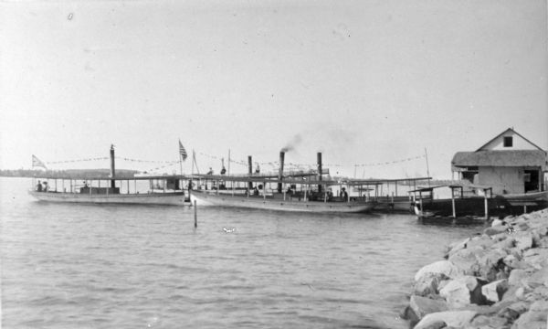 View from shoreline of four boats at the dock for Angle Worm Station: "Tonyawatha," "Lakeside," "Winnequah" and "Monona." People are posing on the boats. A note on the photograph reads: Named after Mrs. Askew, mother of Charles and William Askew who operated the Askew Boat Line, 1872-1927. The Askew brothers purchased Angle Worm Station from Frank Barnes in 1900.