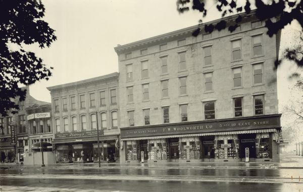 View across street towards the F.W. Woolworth Co. 5 and 10 Cent Store, a large building at 1-5 E. Main Street at the corner of Monona Avenue (now Martin Luther King, Jr., Boulevard). On the left is Harvey's Coats, Suits, Dresses, Shoes, Millinery, Furnishings at 9 E. Main Street, Oetking's  Restaurant, and Uphoff's Coffee Shop.