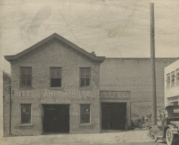 Exterior view of the Ritter Automobile Company located at 212 S. Pinckney Street. Signs on the front read Ritter Automobile Co., Hudson Cars," and "Auto Wash Room." An automobile is parked on the far right.