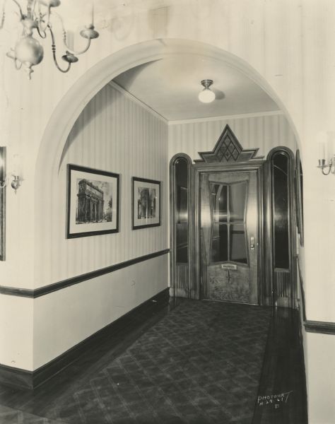 Entrance hall and door of Stanley Hanks' real estate office at 311 State Street. Arched sidelights frame the doorway. Framed prints are on the wall and the floor has a carpet runner.