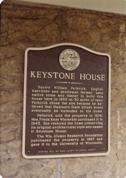 This is number four in Stanley Hanks' collection of four prints of the Keystone House in Shorewood. This is the historical marker erected in 1972 by the Dane County Historical Society. "Squire William Pethrick, English barrister and gentleman farmer, used native stone and timber to build this house here in 1853 on 30 acres of land. 

Pethrick chose the site because he believed that Madison's State Street would eventually be sxtended to his home. Pethrick sold the property in 1876. Mrs. Freda Keys Winterble purchased it in 1943. She restored the home preserving its original architectural style and named it Keystone House. 

The Wis. Alumni Research Foundation purchased the property in 1967 and gave it to the University of Wisconsin."