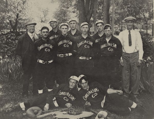Outdoor group portrait of employees of Conklin & Son Company posing in their baseball uniforms. There are nine unidentified baseball players flanked on either side by men wearing suits and hats, probably Mr. Conklin and son. Two of the uniformed players are lying on the ground with bats, balls and mitts in front of them. 

The Conklin Ice House on Lake Mendota existed from about the 1860s until 1936.