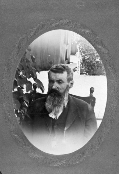 Quarter-length oval-framed portrait of Frank Barnes, in his sixties, sitting in a chair in a garden. He is wearing a suit and vest, and has a moustache and a long beard. Captain Frank Barnes owned and ran the Angle Worm Station on Lake Monona.
