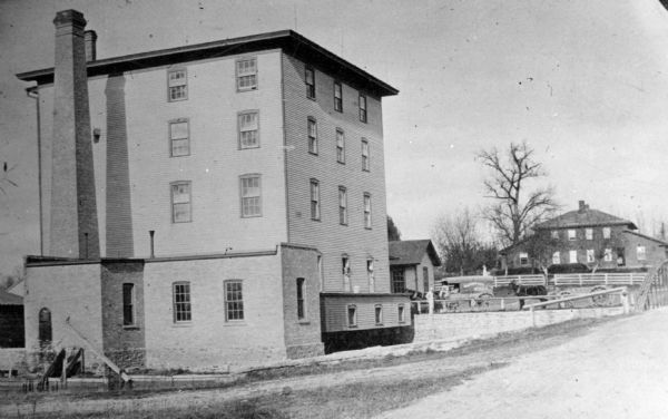 A grist mill on the Yahara River at the outlet of Lake Mendota. The mill, called Farwell's Madison Mills was built in 1850 by Governor Farwell. The original mill burned down in 1873. A horse and wagon in the background reads: "Madison City Mills." The buildings on the right were a brewery owned in 1852 by White and Rodermund. The brewery was eventually sold to Joseph Hausmann and used as a malt house.