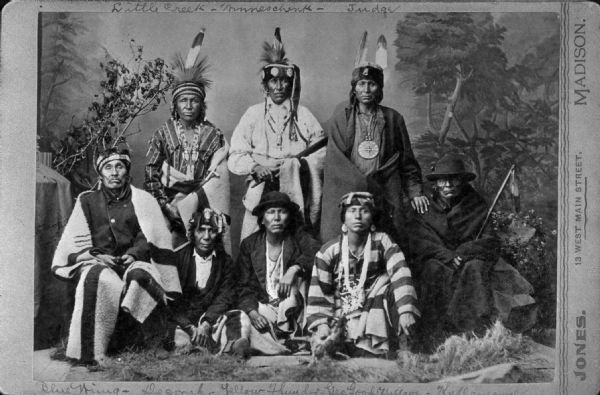 Studio portrait of eight men. From left to right, back row standing: Little Creek — Winneschenk — Judge. Front row: Blue Wing, Decorah, Yellow Thunder, George Good Village, Kella?, and other members of the Black River Indian Band.