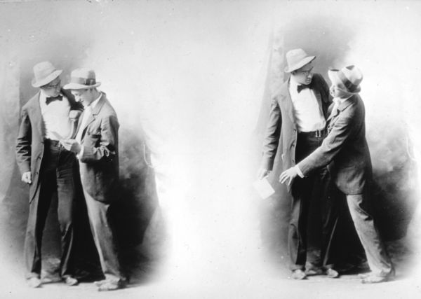 Double portrait, probably in a studio, of two men, in two different poses, one on the left and one on the right. Both men are wearing hats and suits. In the pose on the left, the man on the right is looking at a piece of paper as the man on the left is standing close to him. In the pose on the right, the man on the left is holding the paper and is holding the other man away from it.