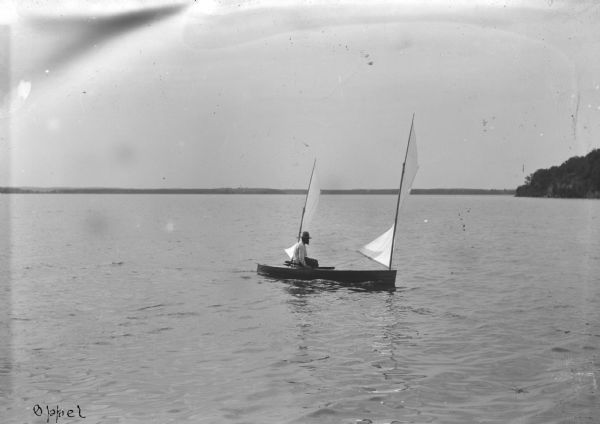 View across water towards Lew Porter, a Madison architect, in a sailing canoe with two sails.