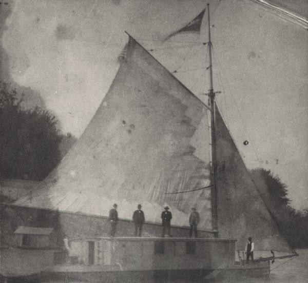The sailboat "Solid Comfort" in full sail, near the shoreline. There are four men standing on top of the cabin. Deckhands are at both ends of the boat. The "Solid Comfort" was jointly owned by M.C. Clarke, D.K. Tenney, Judge Stewart, Philo Dunning, N.B. Van Slyke. Fred Hubbard was deckhand; Jim Vance, cook.