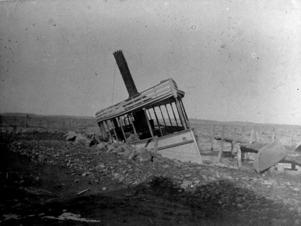 View towards shoreline of a steamboat grounded near a wooden dock. An upside-down canoe or rowboat is propped on the dock. The far shoreline is in the background.