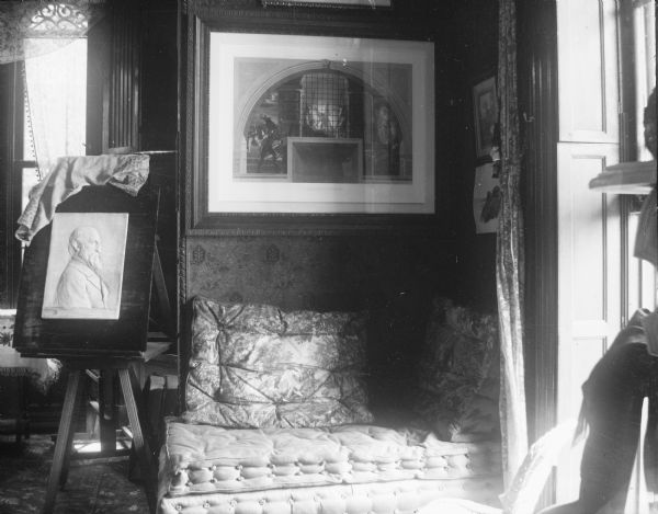 View of a room in the house at 424 N. Pinckney Street. Against one wall is a plush, lounging couch, a portrait on an easel, and flocked wallpaper. There is a large framed print on the wall over the couch. There are windows on the left and right with wooden shutters.

The McDonnell-Garnhart residence, 424 North Pinckney Street. This Romanesque revival house was designed in 1857 by Samuel H. Donnell, the architect for the third Wisconsin Capitol, for contractor Alexander A. McDonnell. The latter used the same Prairie du Chien sandstone that was employed in building the Capitol, a project for which he also served as a contractor that year. 

(Building also known as Pierce House, Garnhardt House, McDonnell House, Mansion Hill Inn.)