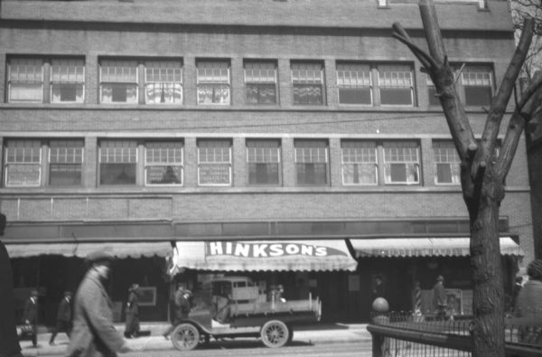 View across street towards Hinkson's, at 644 State Street, which sold malted milk, hot dogs, billiards and smoking material. A truck is parked in front of Hinkson's, and in the right foreground is a fence.