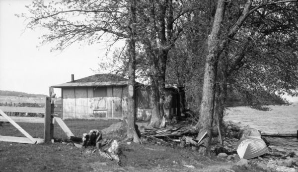 The Stanley Hanks cottage at Fox Bluff on the shore of Lake Mendota. There is a fence around the property, and a boat is pulled up on the shoreline.
