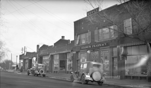 View from street towards the Stadium Pharmacy on the 1500 block of Monroe Street in the Vilas neighborhood. At the far end of the block on the left, at the corner of Regent Street, is a garage and a barbershop.