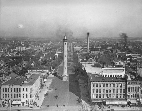 Elevated view from the Wisconsin State Capitol of the old water tower, and an expansive view of the city with church steeples, houses, commercial buildings, and smokestacks. Lake Monona is in the background on the right.
