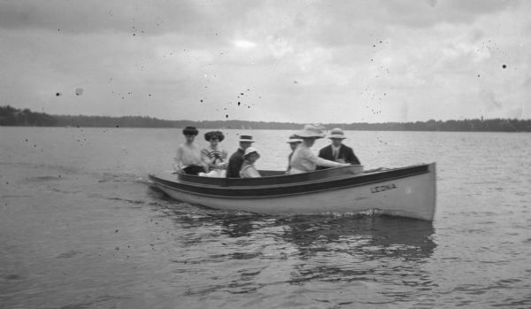 View across water towards a group of people, two men and five women, in a motor boat.