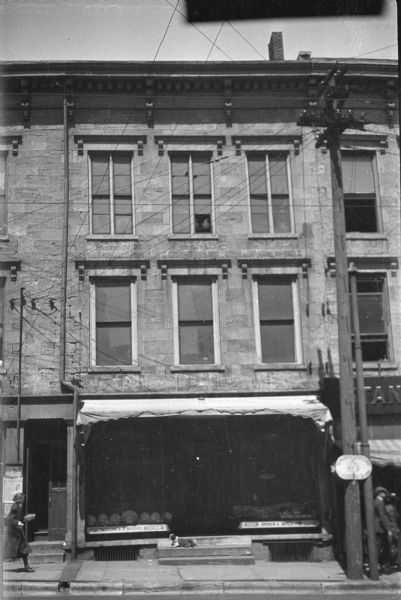 View from street of the storefront in a stone building at 108 King Street. Pedestrians are on the sidewalk,and a dog is sitting on the stoop in front of the entrance.