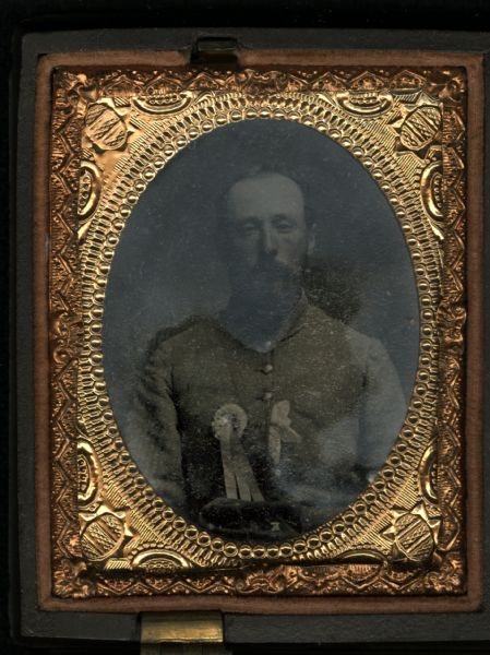 Ninth plate ferrotype/tintype waist-up portrait of a man with moustache and beard. He has ribbons on the front of his chest and a hat resting in his lap. Hand-coloring on cheeks.<p>One image, top left, from a case with four individually oval framed tintypes.</p> 