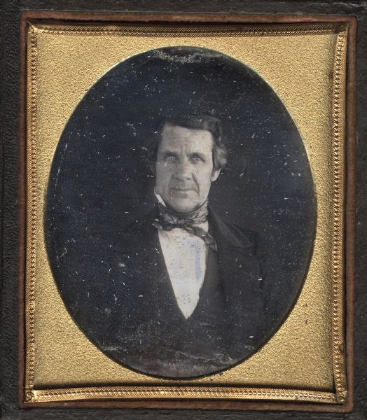 Sixth plate daguerreotype of an unidentified man. Half length portrait facing forward. He wears a suit, stand collar, and cravat. 