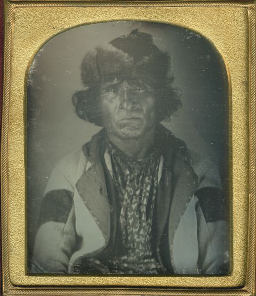 Sixth plate daguerreotype of a waist-up portrait of an unidentified Native American man, possibly from the Canadian Woodland Tribe. He is wearing a coat and a fur hat.